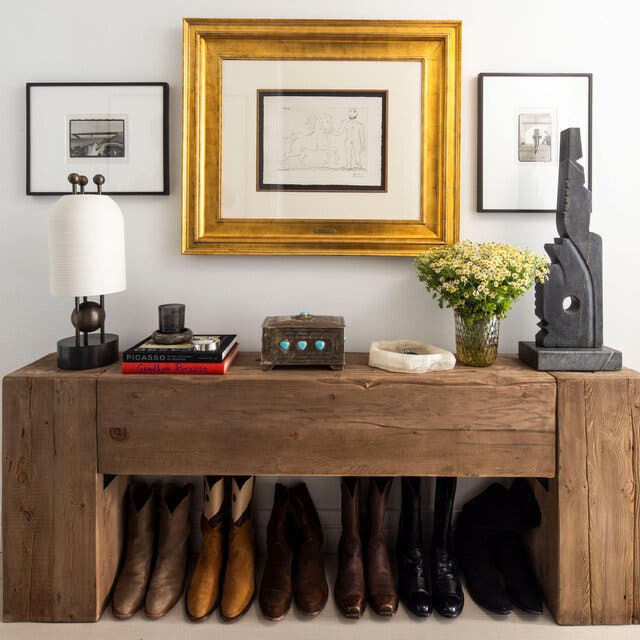 A row of cowboy boots sits on the floor beneath a heavy wood desk. 